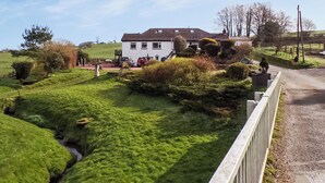 Et hvidt hus med tegltag, omgivet af frodige grønne marker og en lille bæk.
