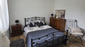 A bedroom with a bed, a dresser, a chair, a nightstand, a lamp, and a painting on the wall. - Private room, in a quiet, leafy setting.  (ploneour lanvern)