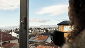 Blick durch ein Fenster, im Vordergrund eine Person, im Hintergrund eine Stadt mit Häusern und Bergen.