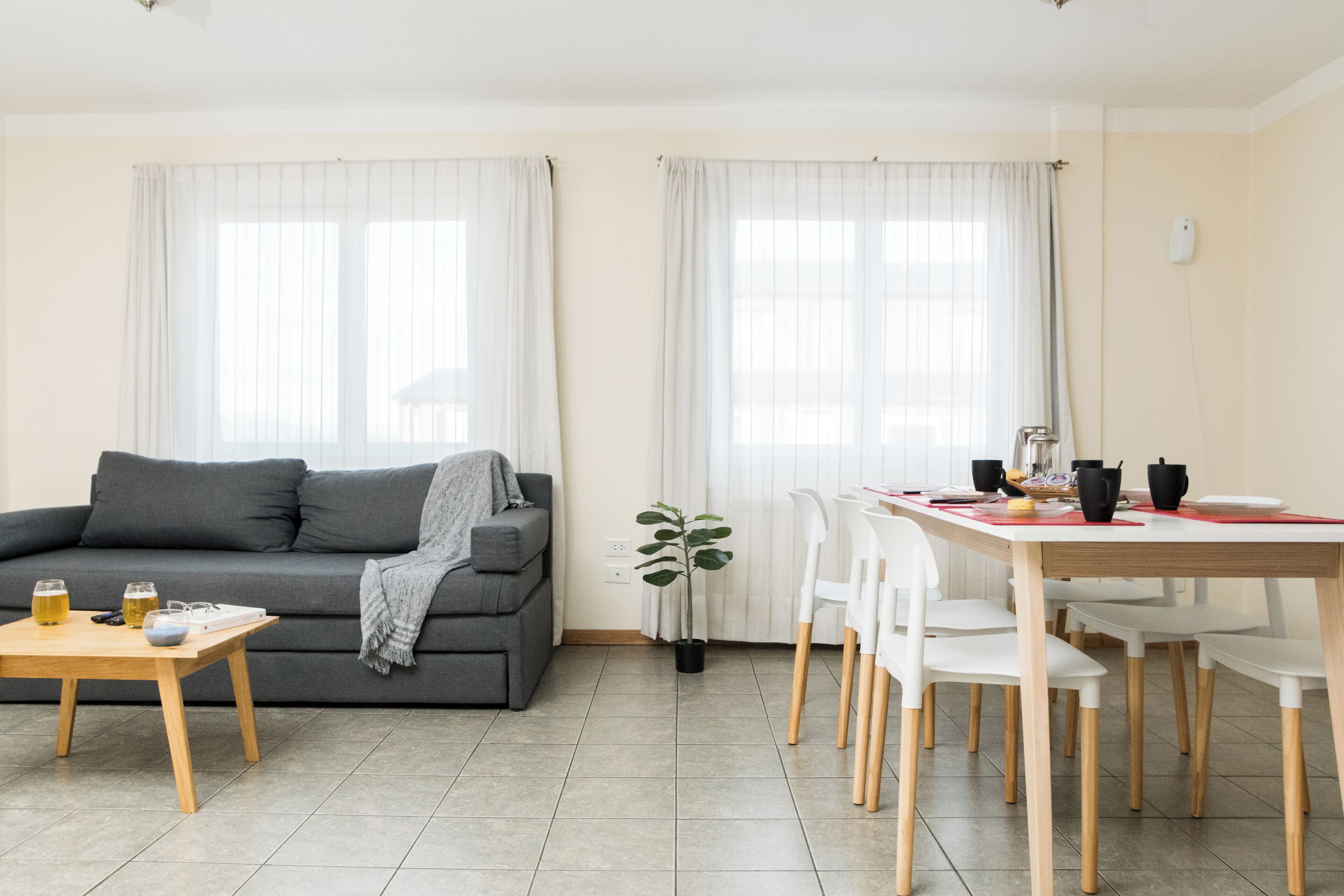 Una sala moderna con un sofá gris, una mesa de centro de madera y una zona de comedor con una mesa y sillas blancas.