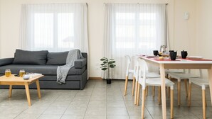 Ein modernes Wohnzimmer mit grauem Sofa, einem Holztisch und einem Essbereich mit weißem Tisch und Stühlen.