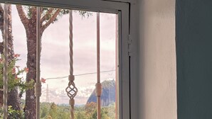A room with a bed, a window with a view of trees and mountains, and a small heater on the windowsill. - Casa De Colores (Guatapé)