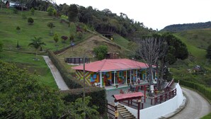 A colorful building with a red roof, surrounded by lush greenery and hills. - Casa De Colores (Guatapé)