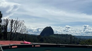 A view from a boat with a large rock formation in the distance, a wooden dock in the foreground, and a cloudy sky. - Casa De Colores (Guatapé)