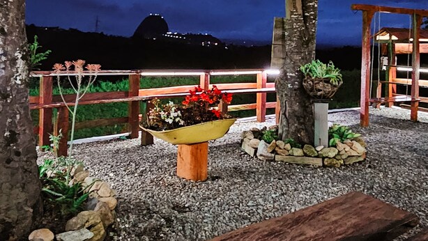 A nighttime outdoor area with a wooden fence, a bench, and a planter with red flowers. - Casa De Colores (Guatapé)