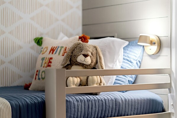 A bed with a plush toy and a pillow with text, a wall-mounted lamp, and a patterned wall.