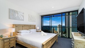 Una habitación de hotel moderna con una cama grande, un cabecero de madera, una mesita de noche con lámpara y un amplio ventanal con vistas a la ciudad.