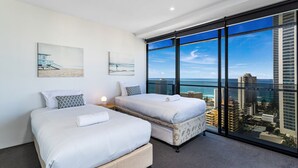 Habitación de hotel moderna con dos camas, ventanas amplias con vistas a la ciudad y obras de arte en las paredes.