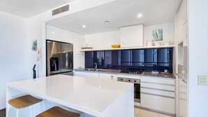 Una cocina moderna con armarios blancos, una isla central con taburetes, electrodomésticos de acero inoxidable y un backsplash azul.
