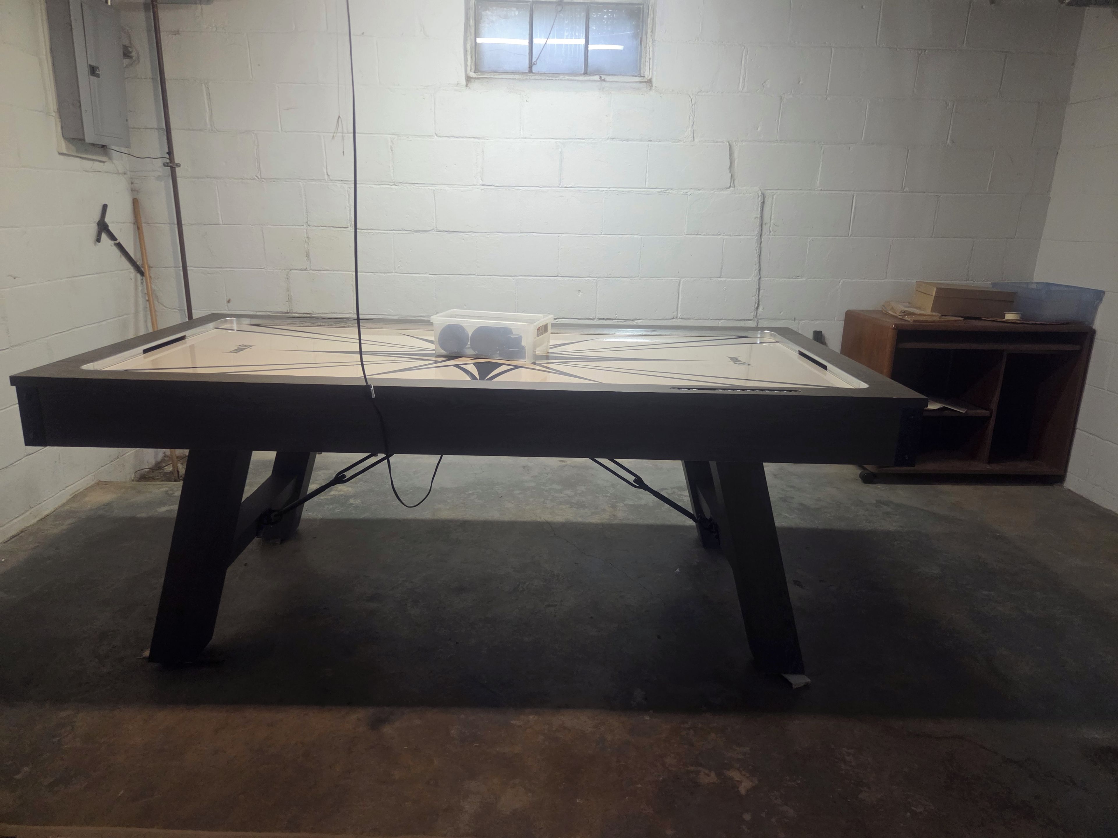 Une table de billard de forme rectangulaire, dotée d’un plateau en verre, est placée dans une pièce aux murs en briques blanches et comportant une fenêtre.