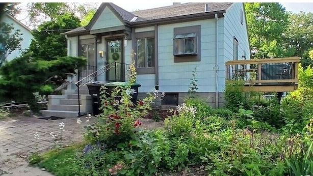 A two-story house with a front porch, a small deck, and a garden with various plants and flowers. - South Omaha Bungalow (Omaha)