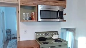 A compact kitchen with a vintage stove, a microwave, and a wooden shelf above. - South Omaha Bungalow (Omaha)