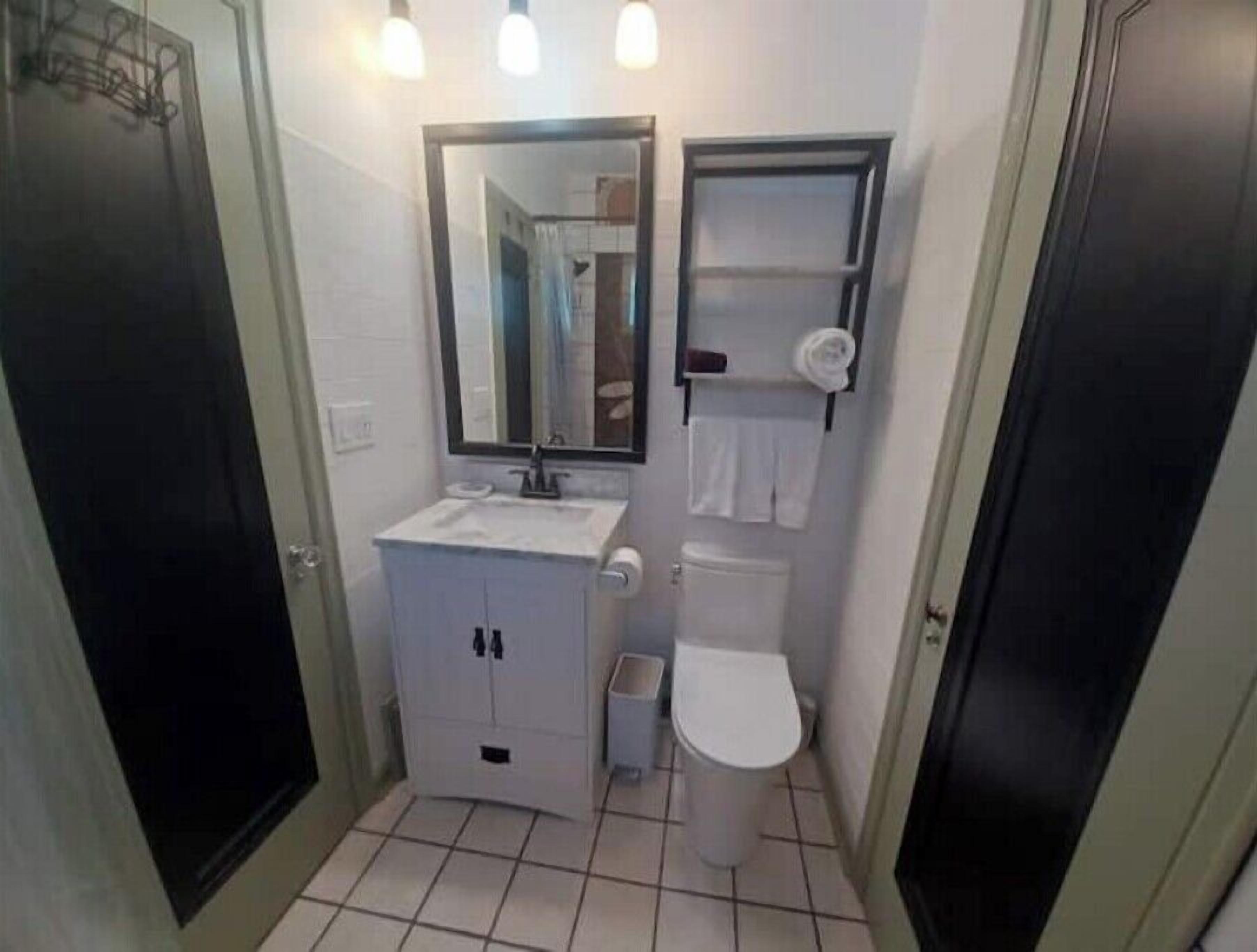 Et lille, kompakt badeværelse med en hvid vask, et spejl, et toilet og en håndklædestang.