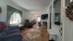 A living room with a sofa, chairs, a TV, and a dining area with a table and chairs. - South Omaha Bungalow (Omaha)