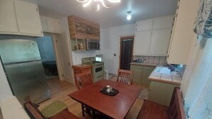 A compact kitchen with a refrigerator, stove, and wooden dining table. - South Omaha Bungalow (Omaha)