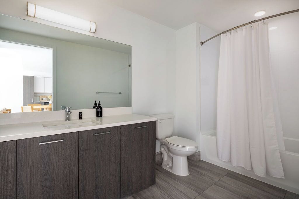 Un baño moderno con cortina de ducha, inodoro y tocador con espejo.