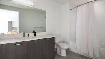 Un baño moderno con cortina de ducha, inodoro y tocador con espejo.
