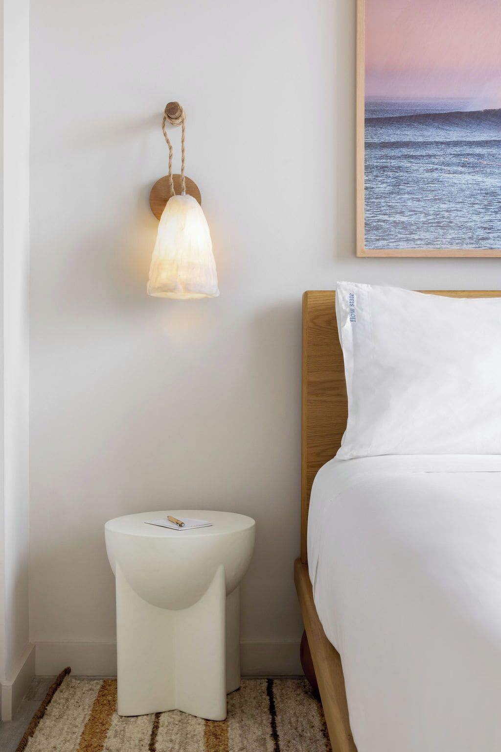 A bedroom with a bed, a bedside table with a lamp, and a wall-mounted picture of the sea.