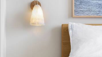 A bedroom with a bed, a bedside table with a lamp, and a wall-mounted picture of the sea.