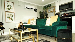 Ein modernes Wohnzimmer mit einem grünen Sofa, einem Glastisch und einem schwarzen Hocker.