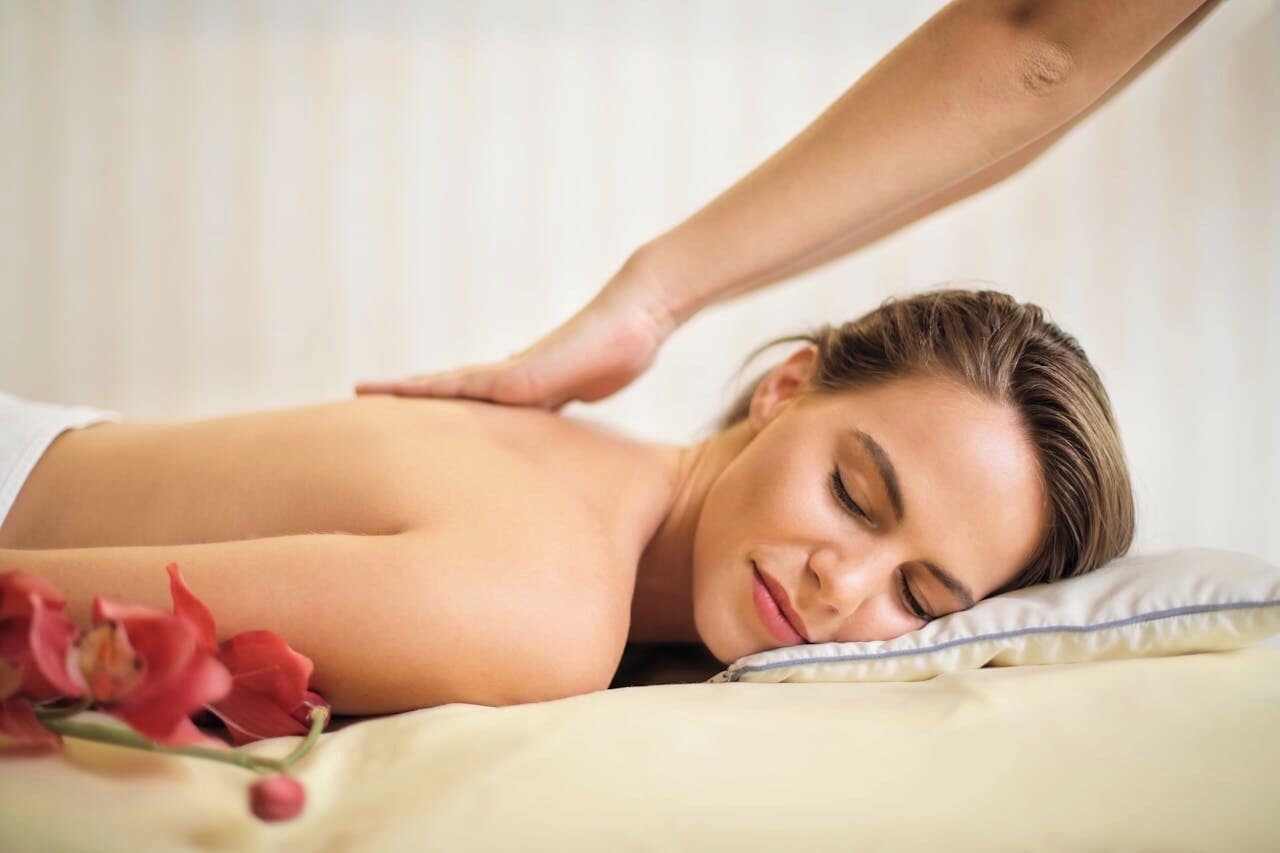 A person receiving a back massage in a room with a bed and a pillow.