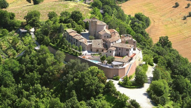 Vue aérienne d’un ensemble de bâtiments historiques entouré d’une végétation luxuriante et de champs.
