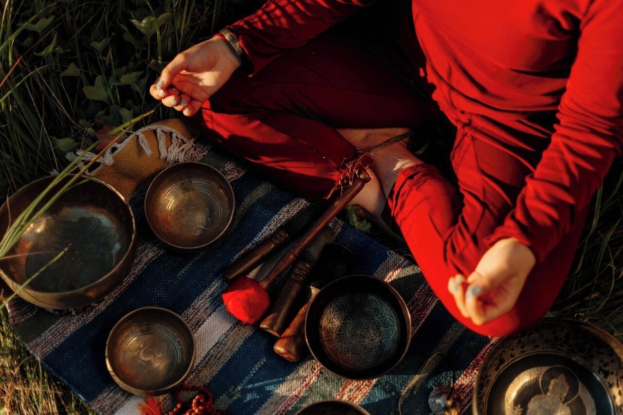 A person sitting on a blanket outdoors with various bowls and a stick.