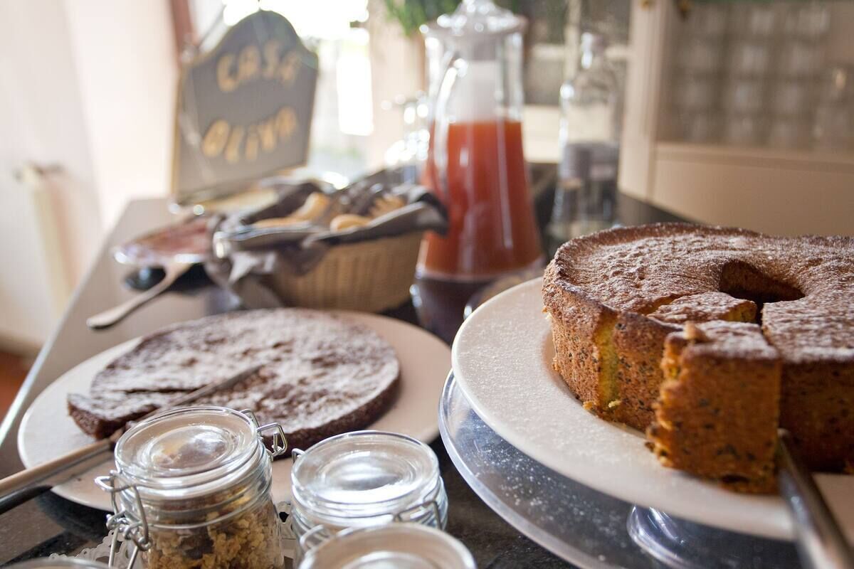 Een tafel met een bundt cake, sneetjes brood, een karaf rode vloeistof en een pot granola.