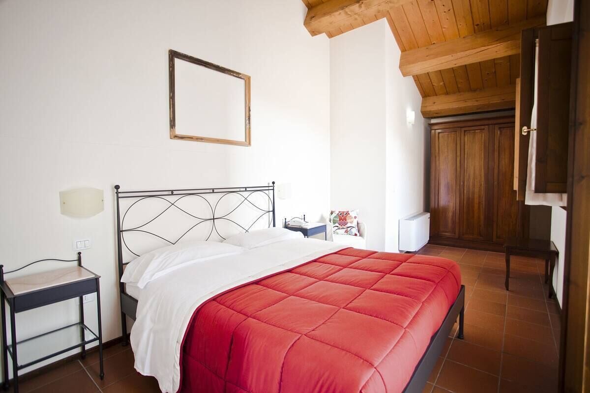 A bedroom with a bed, a bedside table, a nightstand, a wooden wardrobe, and a ceiling with exposed beams.