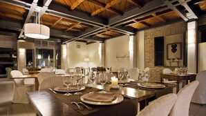 Un espace repas avec une longue table dressée pour un repas, agrémenté de chaises blanches, d’un centre de table composé de bougies et d’un plafond en bois rustique.