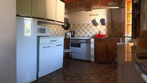 Een kleine keuken met witte apparaten, een betegelde spatwand en een visgraatvloer.