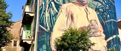 A building with a large mural of a person holding a book, surrounded by greenery.