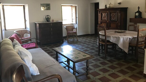 Een woonkamer met een bank, een houten kast, een eettafel met stoelen en een vloer met een patroon.
