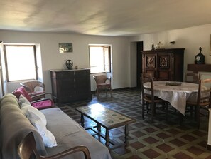 A living room with a sofa, a wooden cabinet, a dining table with chairs, and a patterned floor. - Holiday rentals in Corsica (Luri)