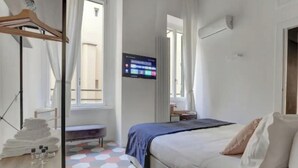Ein Hotelzimmer mit Bett, Wandfernseher, Fenster und Nachttisch mit Handtüchern und Pflegeprodukten.