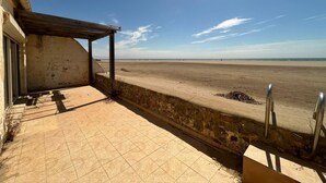 A beach view from a covered patio with a stone wall and metal railing. - House in front of the sea and nature of Fleury (Fleury)