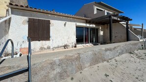 A building with a white exterior, a wooden door, and a window with shutters. - House in front of the sea and nature of Fleury (Fleury)