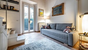 A living room with a sofa, a rug, a lamp, and a painting on the wall.