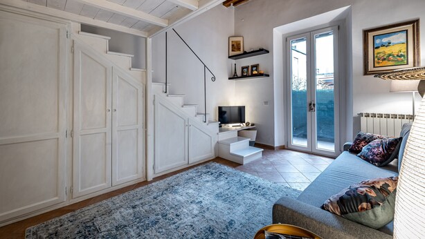 A modern living room with a staircase, a sofa, a flat-screen TV, and a large window.