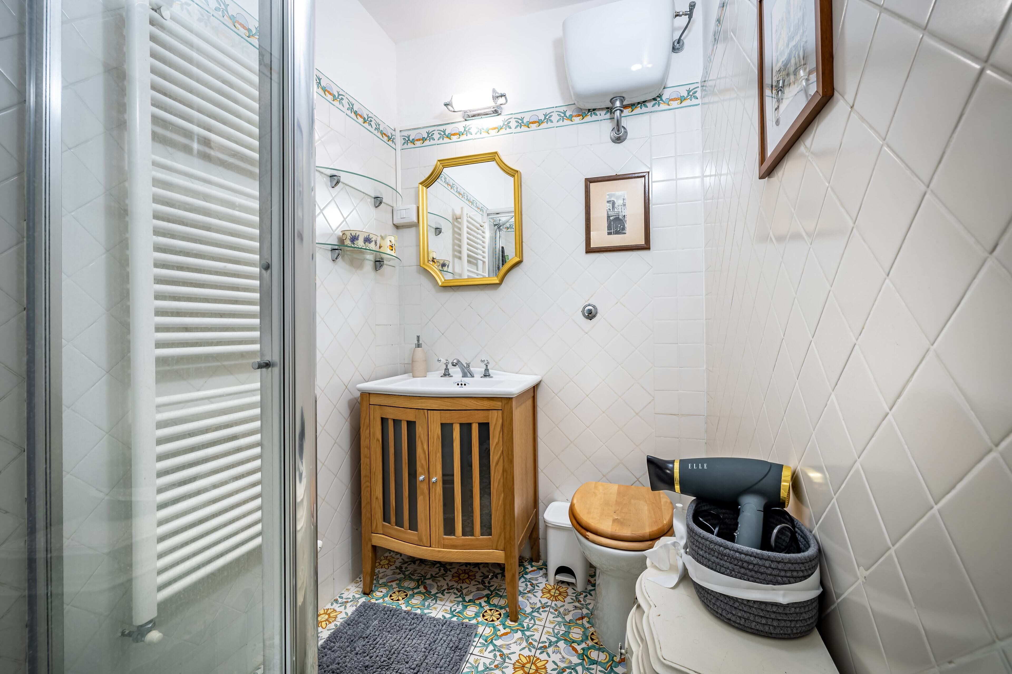 A bathroom with a wooden cabinet, a toilet, a sink, a mirror, and a shower area.