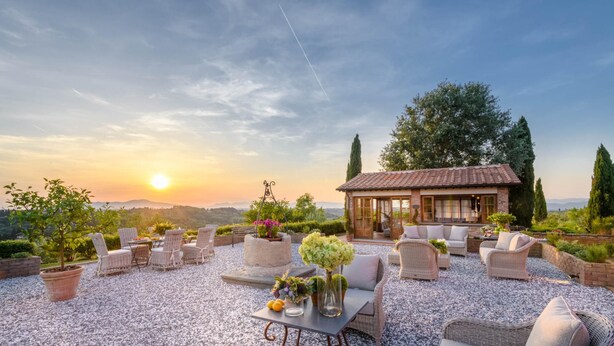 Une terrasse avec des meubles en osier, une table ornée d’un vase et un petit bâtiment doté d’un toit en tuiles.