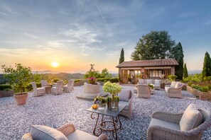 A patio with wicker furniture, a table with a vase, and a small building with a tiled roof. - Villa San Miniato in San Miniato (San Miniato)