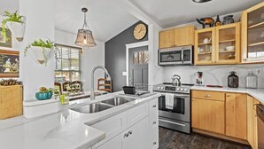 A modern kitchen with white cabinetry, a central island, stainless steel appliances, wooden upper cabinets, and a hanging light fixture. - 3 Bedroom/OnSuite X-Large His & Her Dual Showers bathroom, 5 min to Downtown, Free Large Gated Parking (San Antonio)