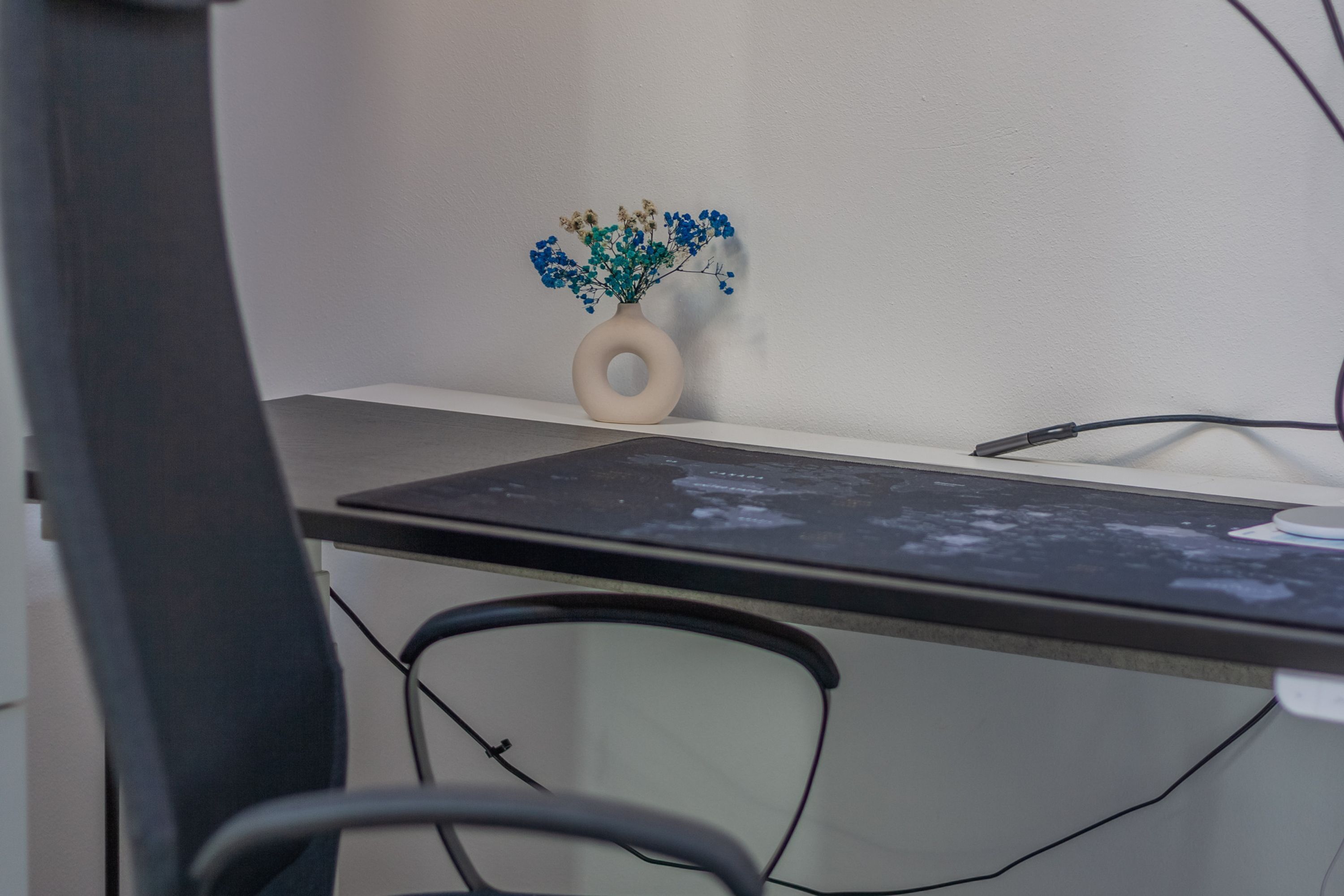 Un bureau avec un vase de fleurs, un écran d’ordinateur et un clavier.