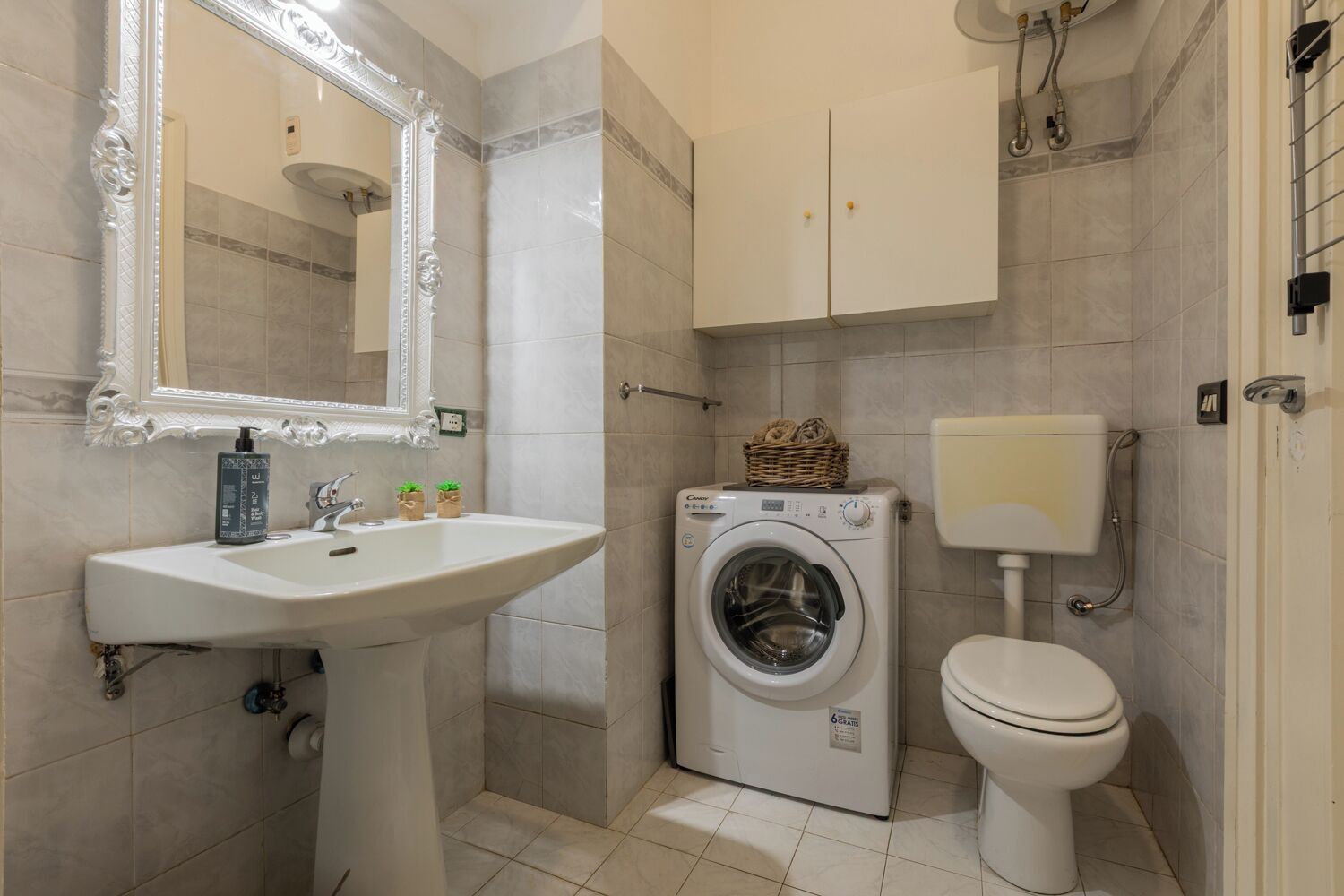 Un baño con lavamanos, lavadora, inodoro y un espejo de marco decorado.