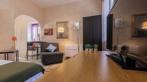 Ein modernes Hotelzimmer mit einem Holztisch, einem bequemen Sessel, einer kleinen Couch, einem Schreibtisch mit Stuhl und einem großen Spiegel.