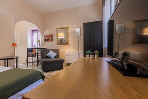 Una camera d'albergo moderna con un tavolo da pranzo in legno, una poltrona comoda, un piccolo divano, una scrivania con una sedia e un grande specchio.