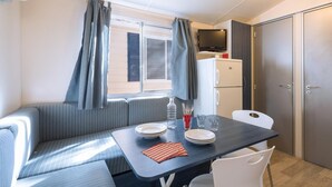 Una kitchenette compacta con refrigerador, televisor y comedor con mesa y sillas.