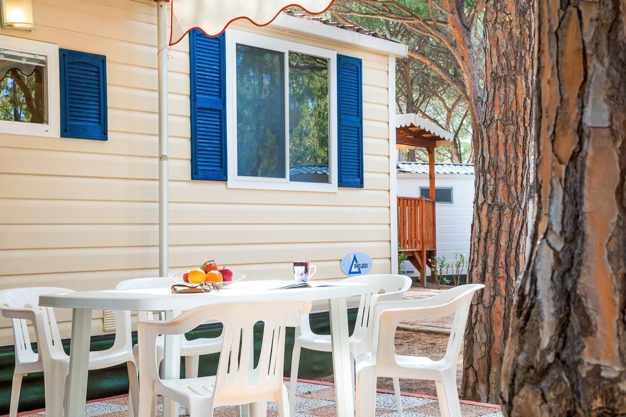 A white table with plastic chairs, a fruit bowl, and a sign reading "SHELBOX".
