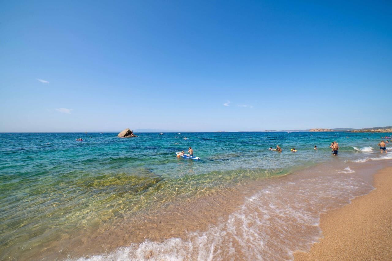 A beach with clear water, people swimming and surfing, and a sandy shore.